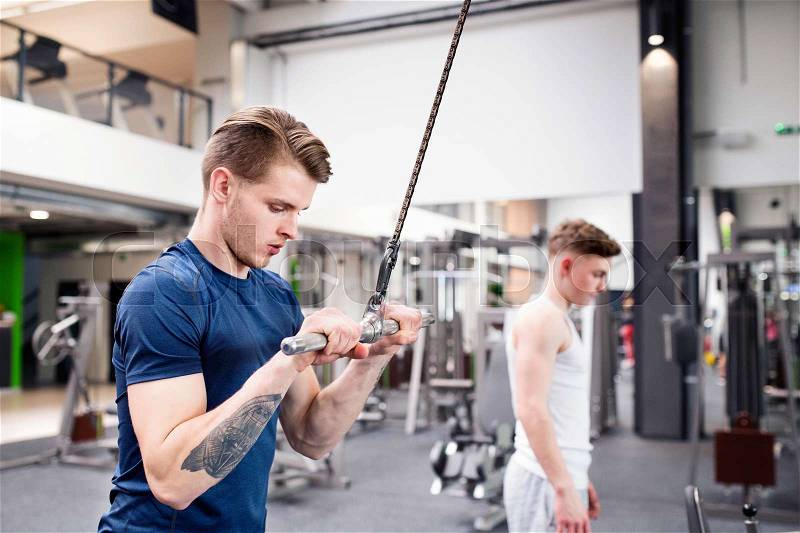 Young handsome fit man working out on pull-down machine in gym. Bodybuilder exercising with cable weight machine, stock photo