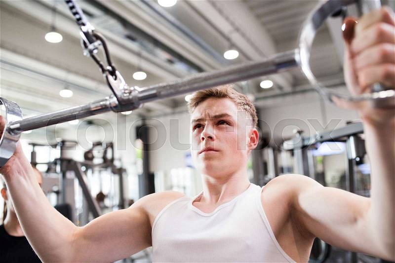 Young handsome fit man working out on pull-down machine in gym. Bodybuilder exercising with cable weight machine. Close up, stock photo