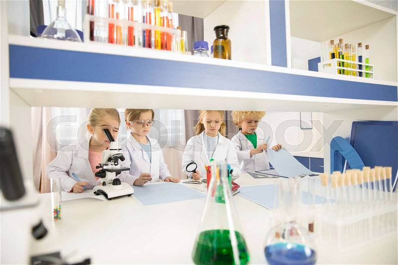 Schoolchildren in lab coats studying together in chemical laboratory , stock photo