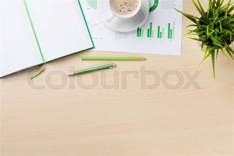 Office desk workplace with charts, coffee cup, plant and notepad on wooden table. Top view with copy space, stock photo
