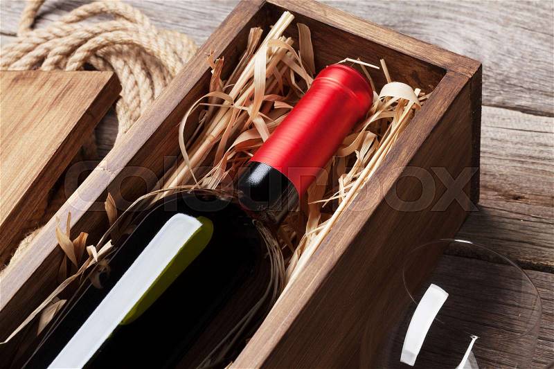 Red wine bottle in box and glass on wooden table, stock photo