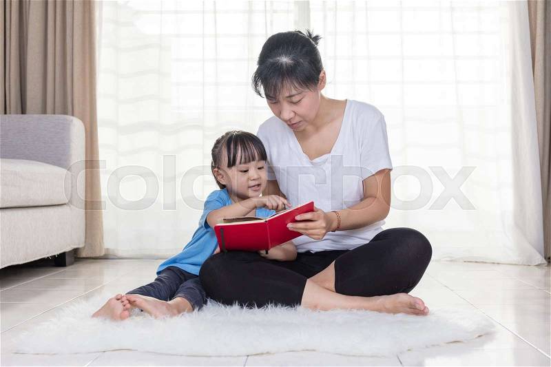Asian Chinese mother and daughter reading on the floor at home, stock photo