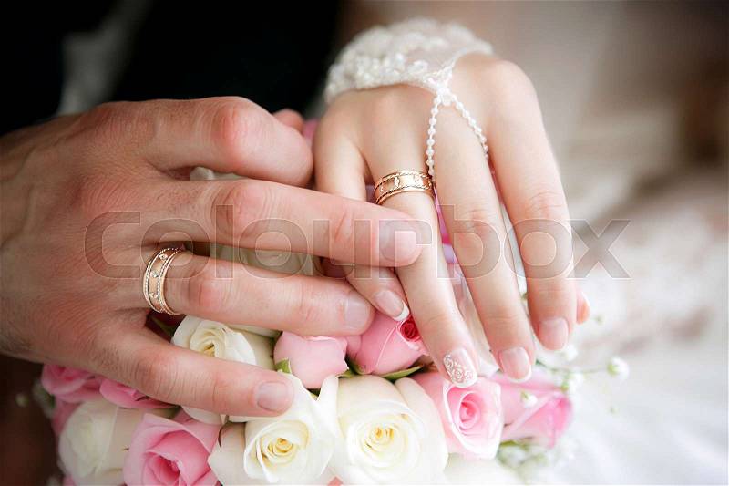 Hands of the groom and the bride with wedding rings and a wedding bouquet from roses, stock photo
