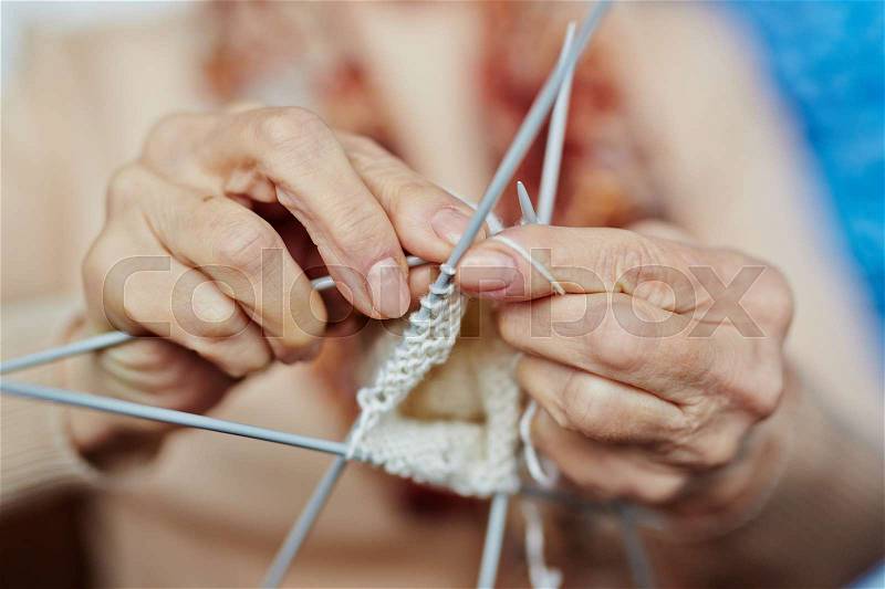 Senior woman knitting warm sweater for her son with white wool, close-up shot, stock photo