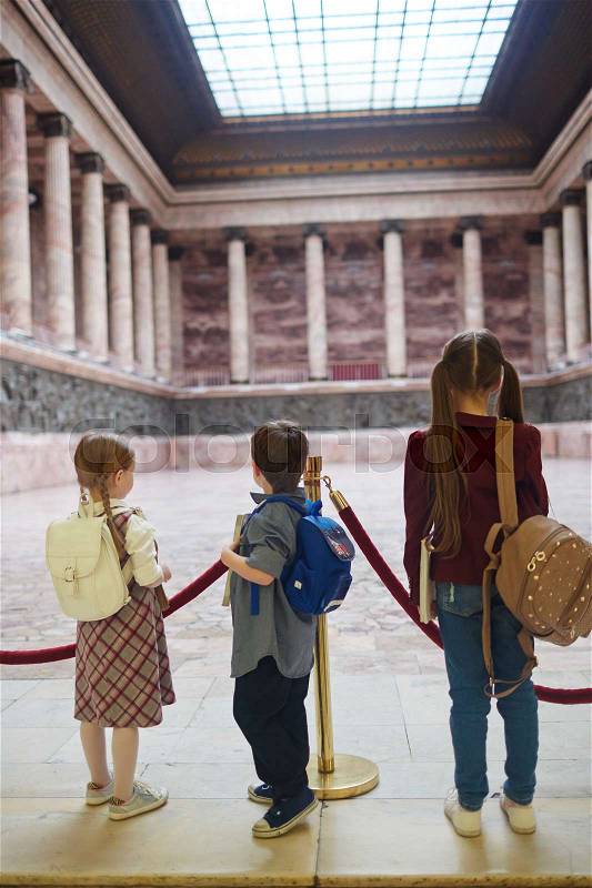 Three schoolkids with backpacks visiting modern museum, stock photo