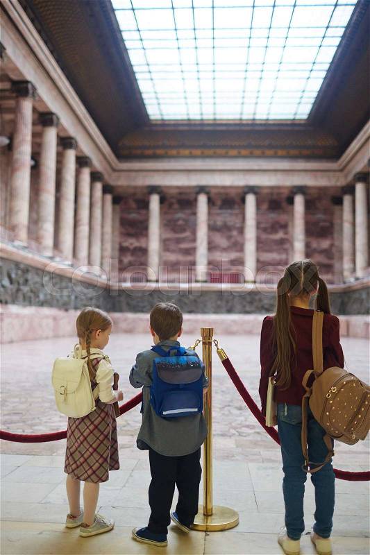 Group of friendly kids with school-bags standing in museum, stock photo