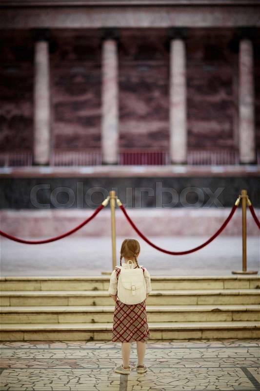 Little schoolgirl standing by red velvet rope in museum, stock photo