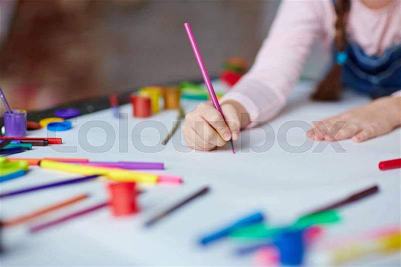 Little girl holding crayon or highlighter on paper, stock photo