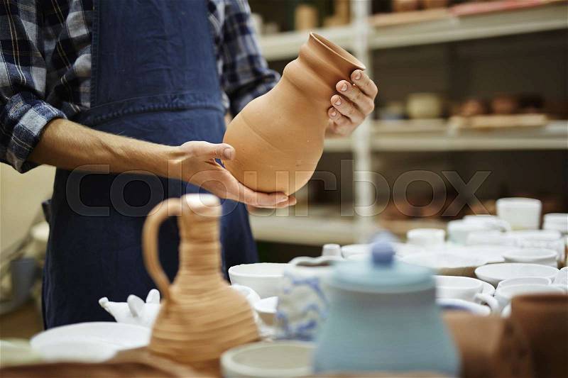 Young craftsman holding jug over collection of crockery, stock photo