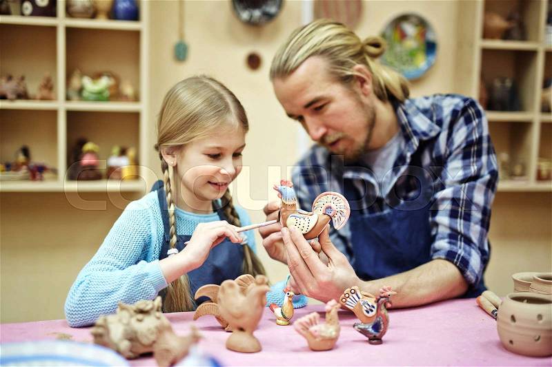 Young man showing his daughter how to paint clay toys, stock photo