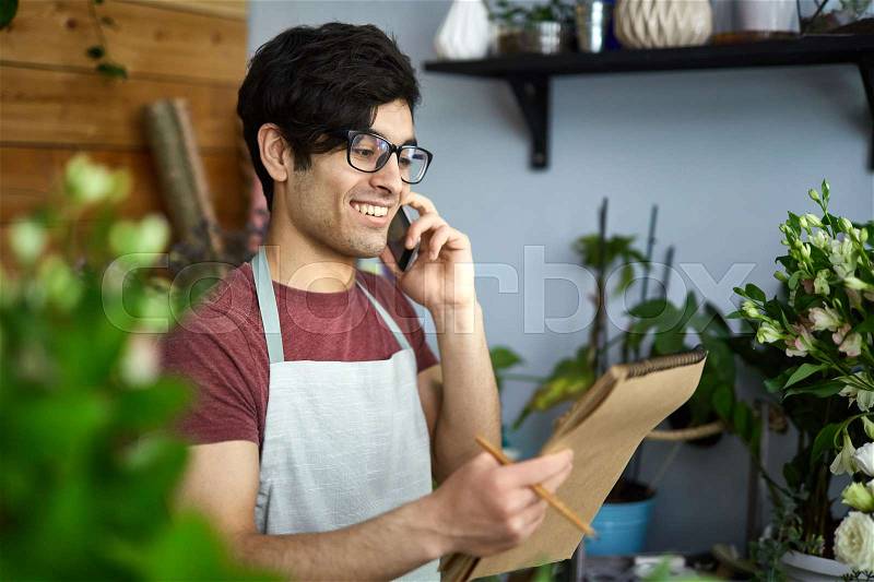Young florist talking to client on smartphone, stock photo