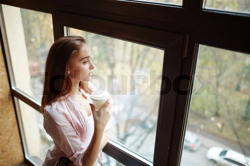 Girl with plastic glass standing by window, stock photo