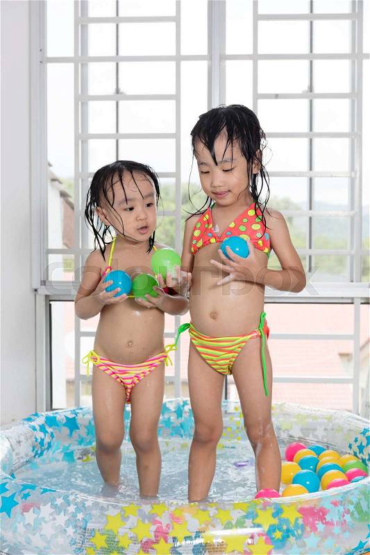 Happy Asian Chinese little sisters playing in the inflatable pool inside the house, stock photo