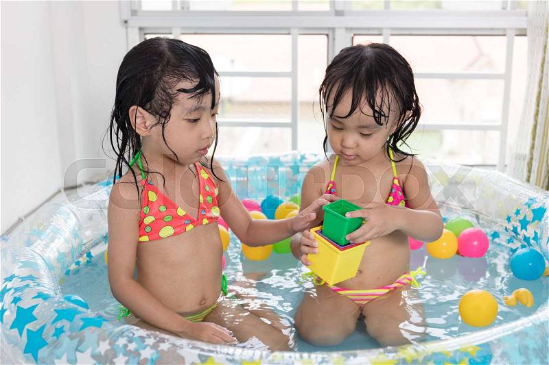 Asian Chinese little sisters playing in the inflatable pool inside the house, stock photo