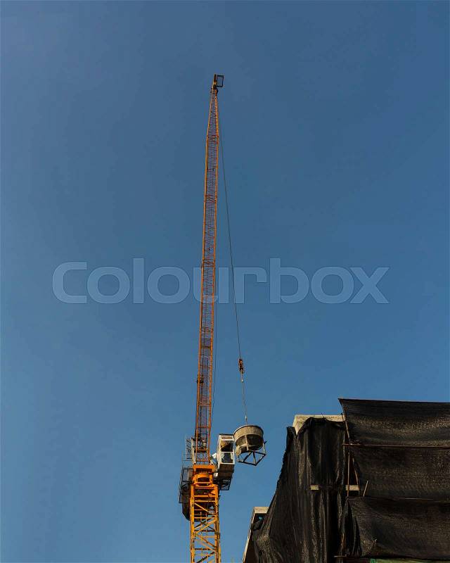 Tower crane lift cement bucket up to top of building during construcion with blue sky background, stock photo