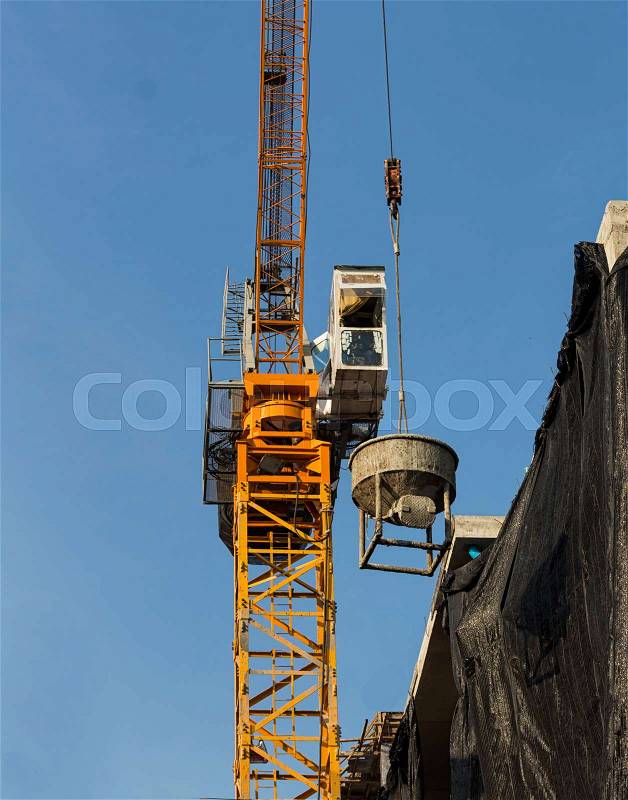 Tower crane lift cement bucket up to top of building during construcion with blue sky background, stock photo