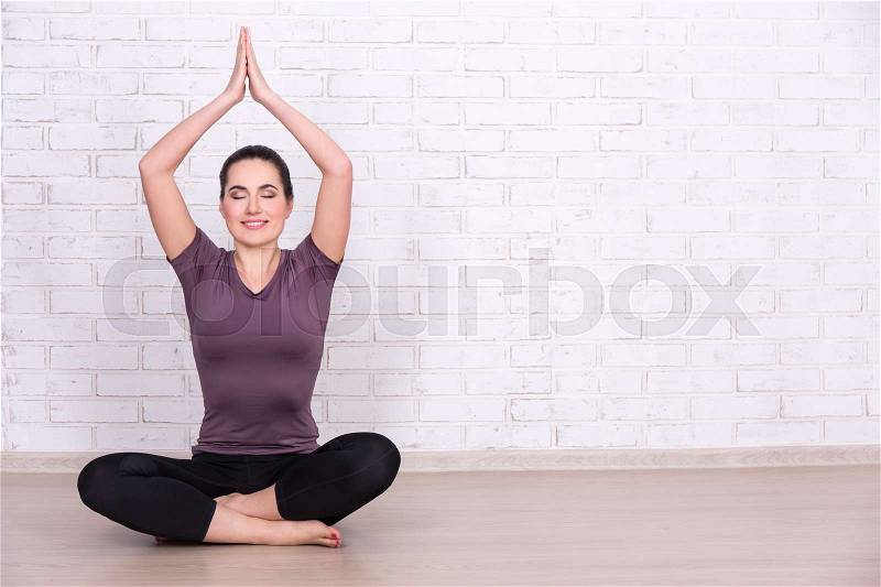 Slim sporty woman doing yoga over white brick wall background, stock photo