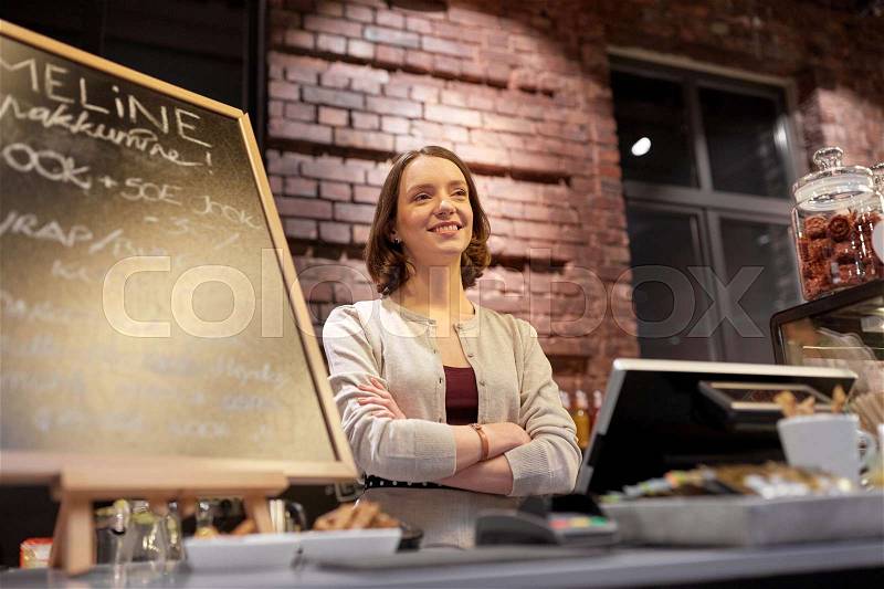 Small business, people and service concept - happy woman or barmaid at counter with cashbox in cafe or coffee shop, stock photo