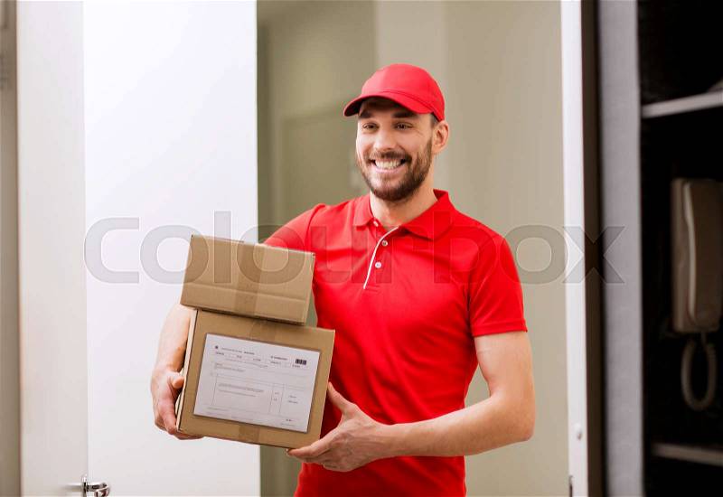 Delivery, mail, people and shipment concept - happy man in red uniform with parcel boxes in corridor at open customer door, stock photo