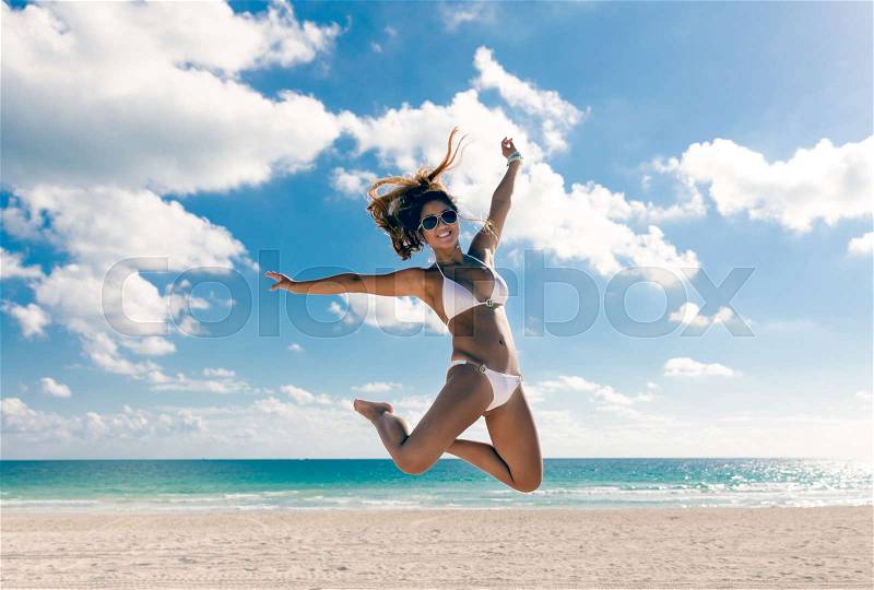 Happy bikini asian woman jumping of joy on beach. Tropical vacation travel destination, stock photo