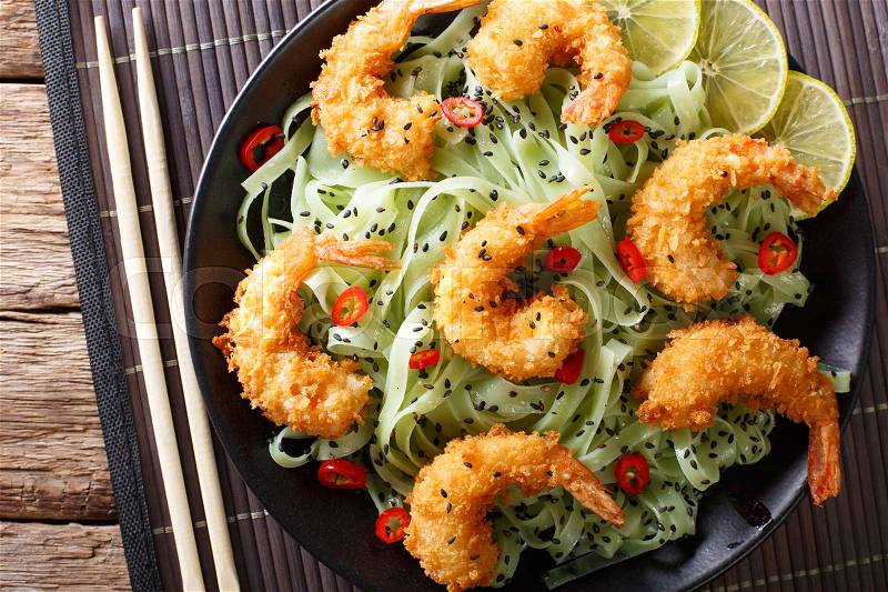 Fried Shrimp in breadcrumbs with green pasta and sesame close-up on a plate. horizontal view from above , stock photo