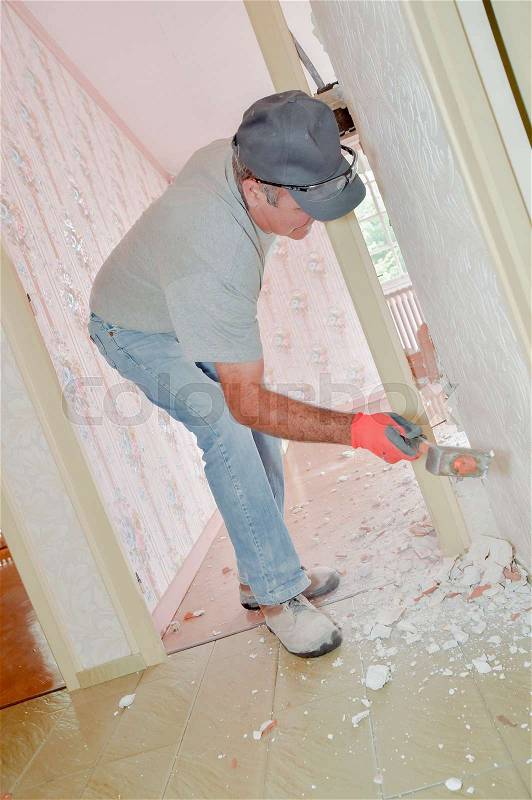 Builder knocking down partition wall with sledgehammer, stock photo