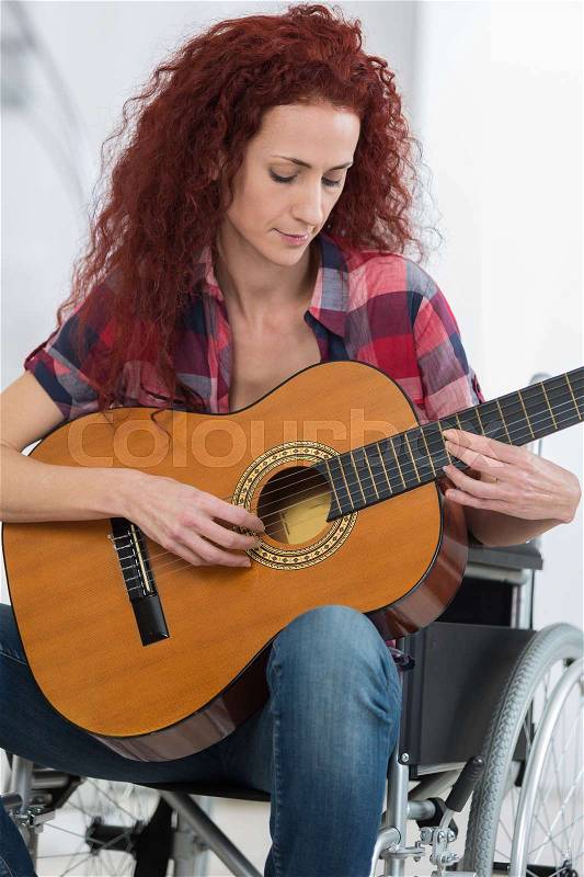 Disabled woman playing guitar in her living room, stock photo