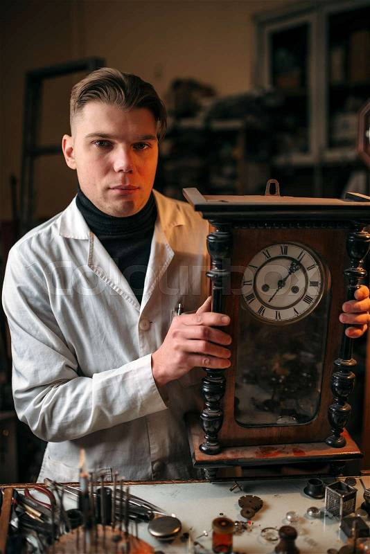 Watchmaker adjusts the mechanism of old wall clock in the workshop, stock photo