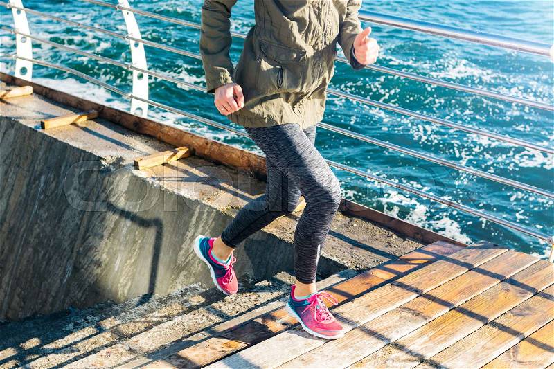 Athletic woman in sports clothes runs up the stairs in sneakers against the background of the sea. Sunny morning, a healthy lifestyle outdoors, stock photo