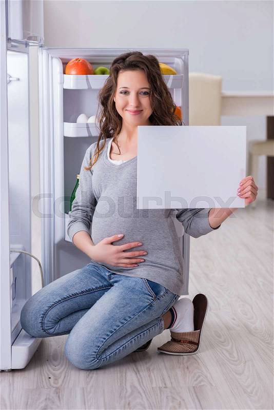 Pregnant woman near fridge with blank message, stock photo