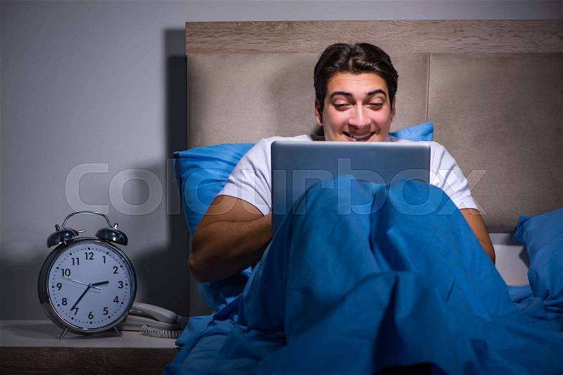 Young man working on laptop in bed, stock photo