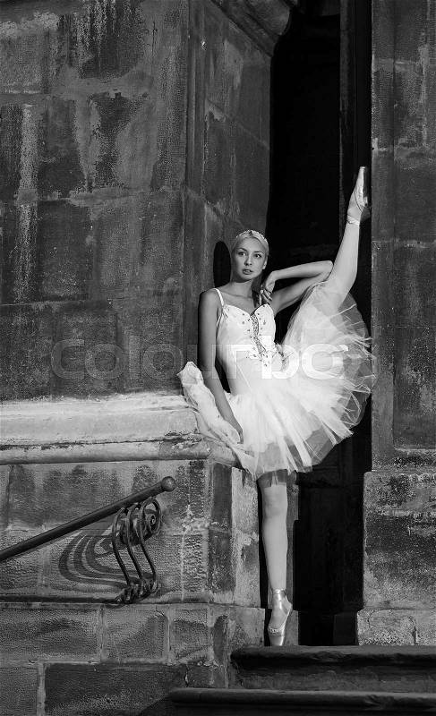Thoughtful grace. Vertical monochrome shot of a young ballerina posing with her leg up against the wall soft focus, stock photo