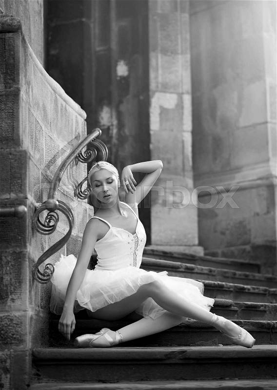 Embodying femininity. Monochrome shot of a beautiful ballerina sitting on stairs near an old building soft focus, stock photo