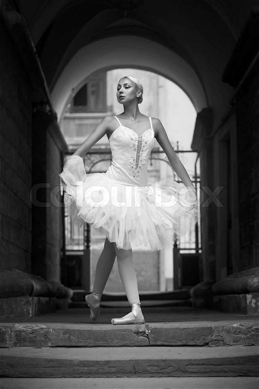 Dancing on the streets. Monochrome portrait of a beautiful ballerina standing in an archway , stock photo