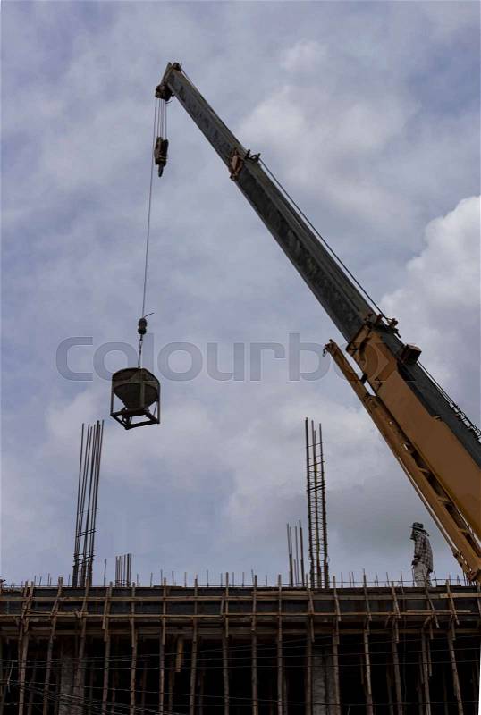 Tower crane lift cement bucket up to top of building during construcion with cloudy sky background, stock photo