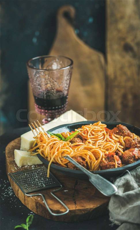 Italian pasta dinner. Spaghetti with meatballas, basil and parmesan cheese in black plate and red wine in glass on wooden board, selective focus. Slow food concept, stock photo