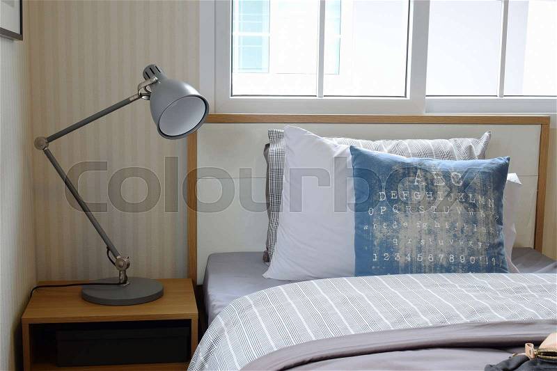 Cozy bedroom interior with pillows and reading lamp on bedside table, stock photo
