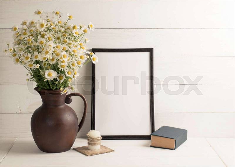 Daisy bouquet in clay jug with motivational frame, book and candle on background of white wooden planks in scandinavian style. Home interior, stock photo