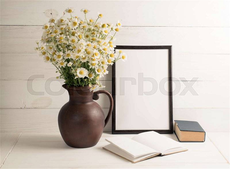 Daisy bouquet in clay jug with motivational frame and open notebook on background of white wooden planks in scandinavian style. Home interior, stock photo