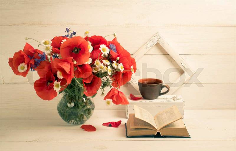 Red poppies bouquet in round vase, open book, tea cup and photo frame on background of white wooden planks in scandinavian style, stock photo