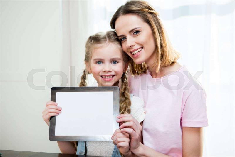 Happy mother and daughter showing digital tablet at home, stock photo