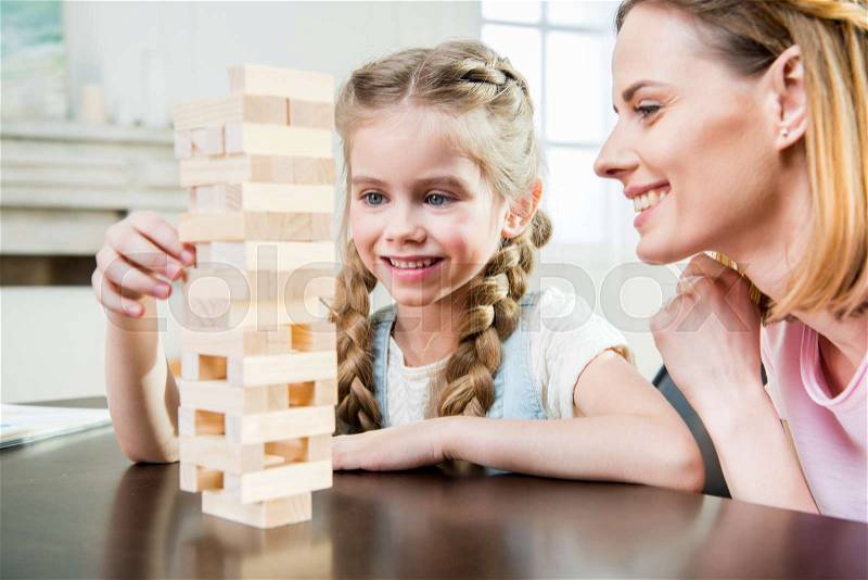 Happy mother and daughter playing jenga game on table at home , stock photo