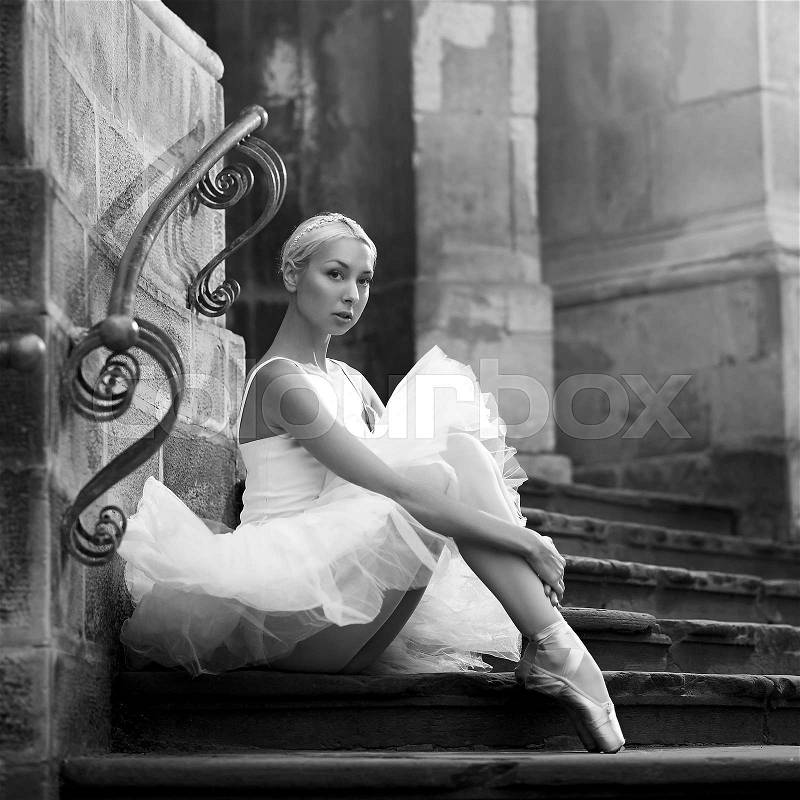 So untouched and innocent. Monochrome portrait of a beautiful ballerina wearing white sitting on the stairs of an old castle , stock photo