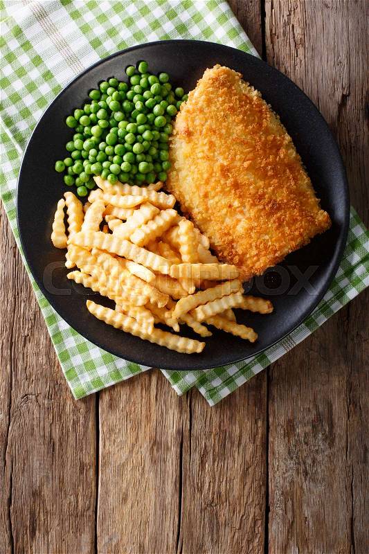Traditional British food: Fish and chips with green peas close-up on a plate on a table. Vertical view from above , stock photo