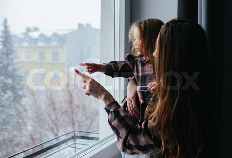 Mom with little girl looking through the window, winter, stock photo