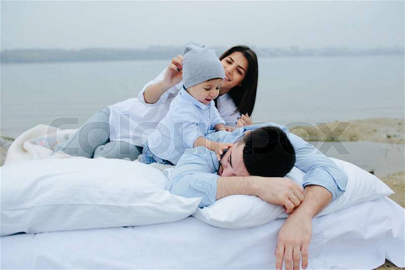 Happy young family relaxing together on the lake. They lie on a white mattress with pillows, stock photo