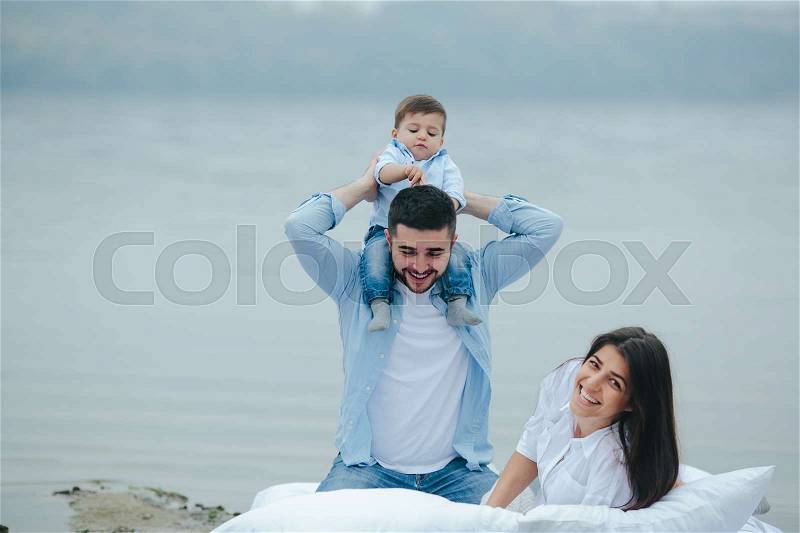 Happy young family relaxing together on the lake. They lie on a white mattress with pillows, stock photo