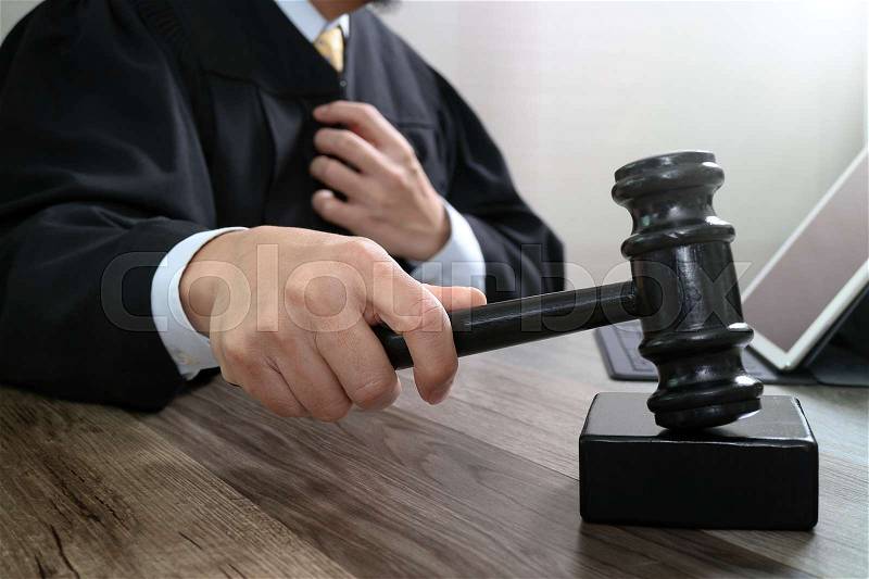 Justice and law concept.Male judge in a courtroom striking the gavel,working with digital tablet computer docking keyboard on wood table, stock photo