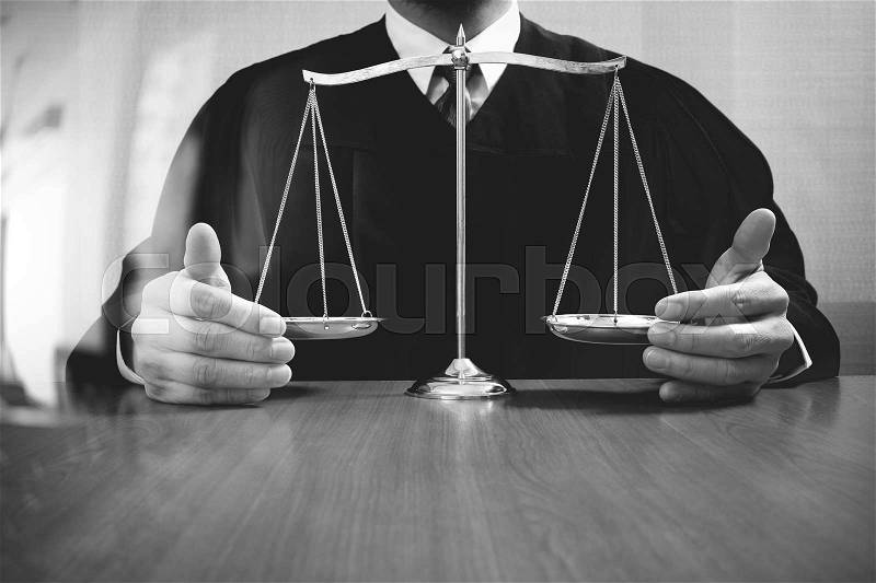 Justice and law concept.Male judge in a courtroom with the balance scale on wood table,black and white, stock photo