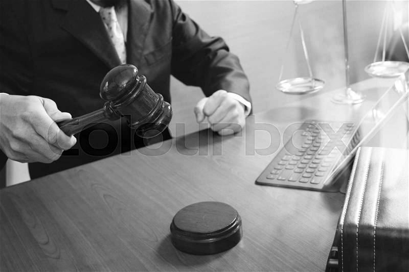 Justice and law concept.Male judge in a courtroom with the gavel,working with smart phone,digital tablet computer docking keyboard,brass scale,on wood table,black and white, stock photo